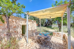 Un patio al aire libre con una mesa dispuesta para dos personas, una pérgola sobre la cabeza y un muro de piedra.