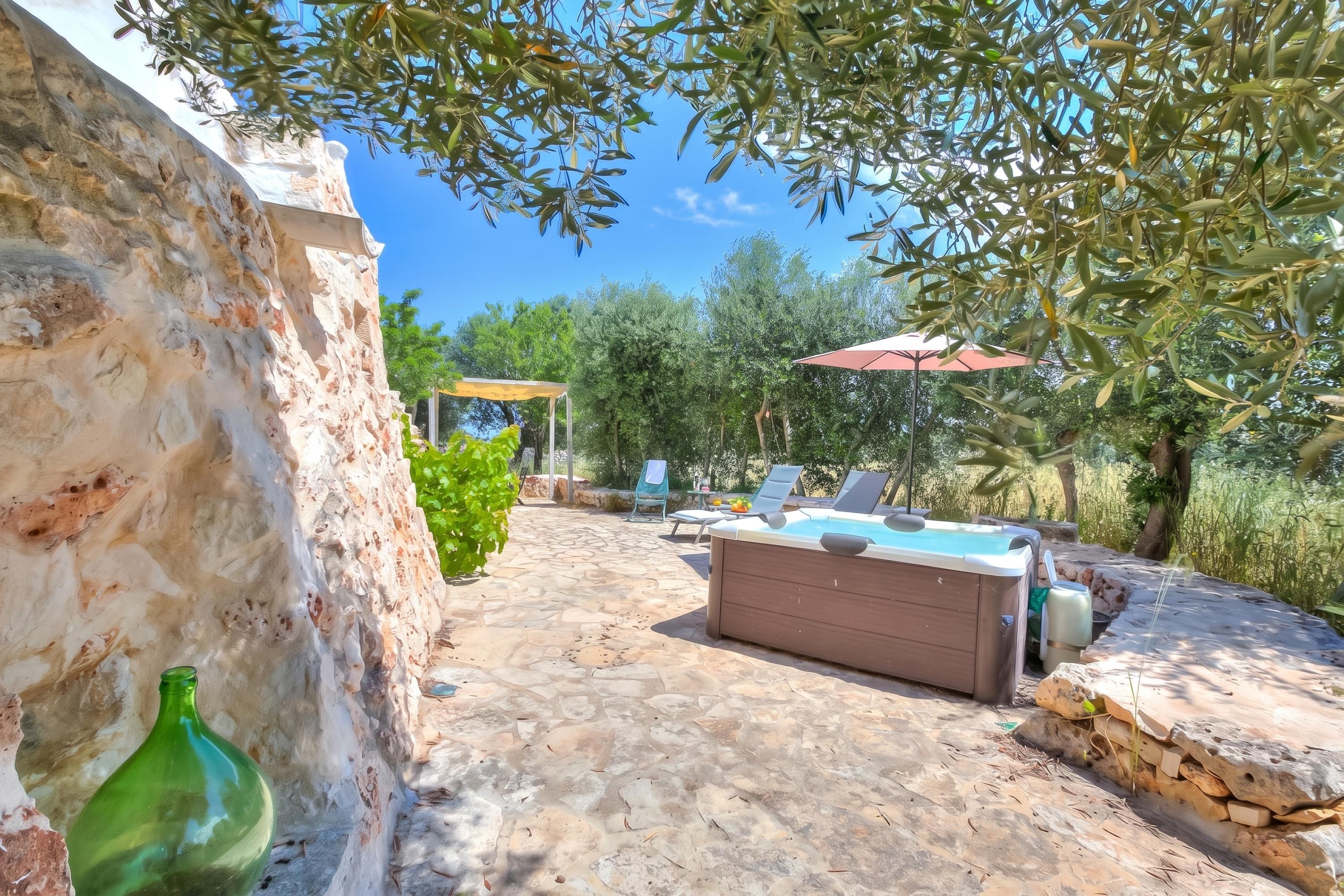 Une terrasse en pierre avec un jacuzzi, des chaises longues et une pergola surmontée d’un parasol rouge.