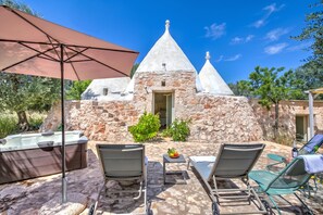 A stone building with a conical roof, outdoor seating with chairs and a table, and a hot tub. - Dimora Tra Gli Ulivi With Private Jacuzzi (Ostuni)