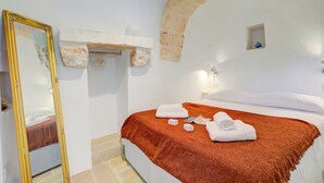 Een slaapkamer met een groot bed, een spiegel, een stenen muur en een klein raam.