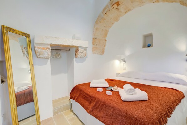 Un dormitorio con una cama grande, un espejo, una pared de piedra y un ventanal pequeño.
