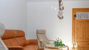 Ein modernes Wohnzimmer mit einer Couch, einem Sessel, einem kleinen Tisch mit einer Pflanze und einer Holztür.
