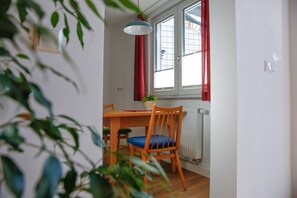 Ein Essbereich mit Tisch, Stühlen, einer Pendelleuchte, einem Fenster mit roten Vorhängen und einer Heizung.