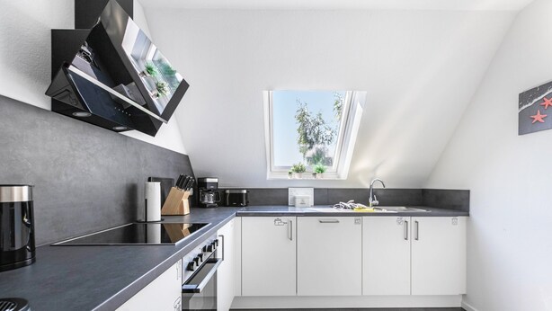 Een moderne keuken met een inbouwoven, een koffiezetapparaat en een raam met uitzicht op groen.