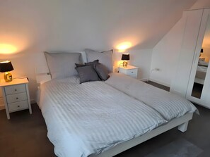 A bedroom with a large bed, two bedside tables with lamps, a wardrobe, and a sloped ceiling.