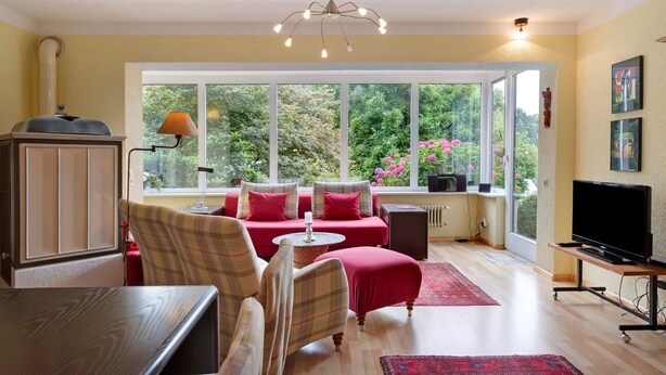 A room with a sofa set, a television, a table, and a window with a view of greenery. - Apartment 'Kneissler' with Mountain View, Private Terrace and Wi-Fi (Oberried)