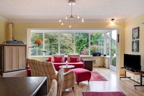 Une pièce comprenant un canapé, un téléviseur, une table et une fenêtre donnant sur un paysage verdoyant.