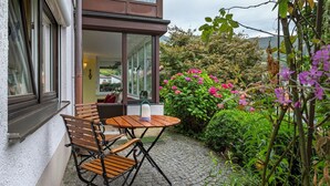 A patio with a table and chairs, a lamp, and a view of a garden with pink flowers. - Apartment 'Kneissler' with Mountain View, Private Terrace and Wi-Fi (Oberried)