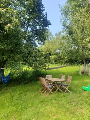 Un espace extérieur verdoyant avec une table et des chaises en bois, un hamac et un toboggan vert.