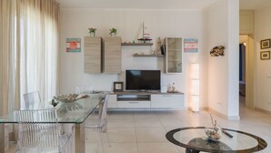 En moderne stue med et glasbord, transparente stole, et fladskærms-tv og minimalistisk indretning.