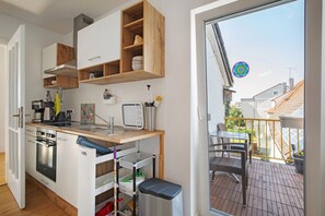 Et kompakt køkken med indbyggede apparater, træhylder og udsigt til den udendørs balkon.