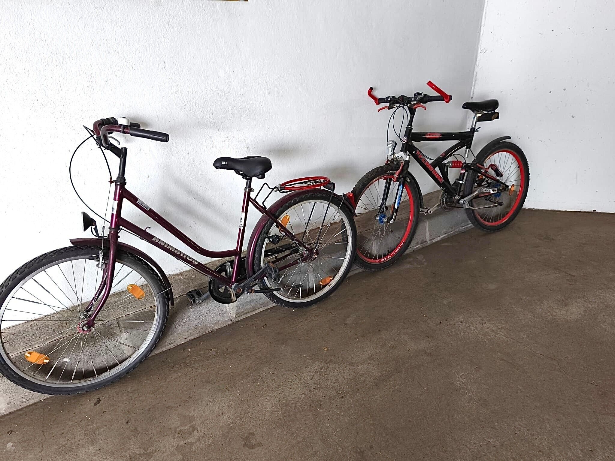 Zwei Fahrräder lehnen an einer Wand in einem Raum mit Betonboden.