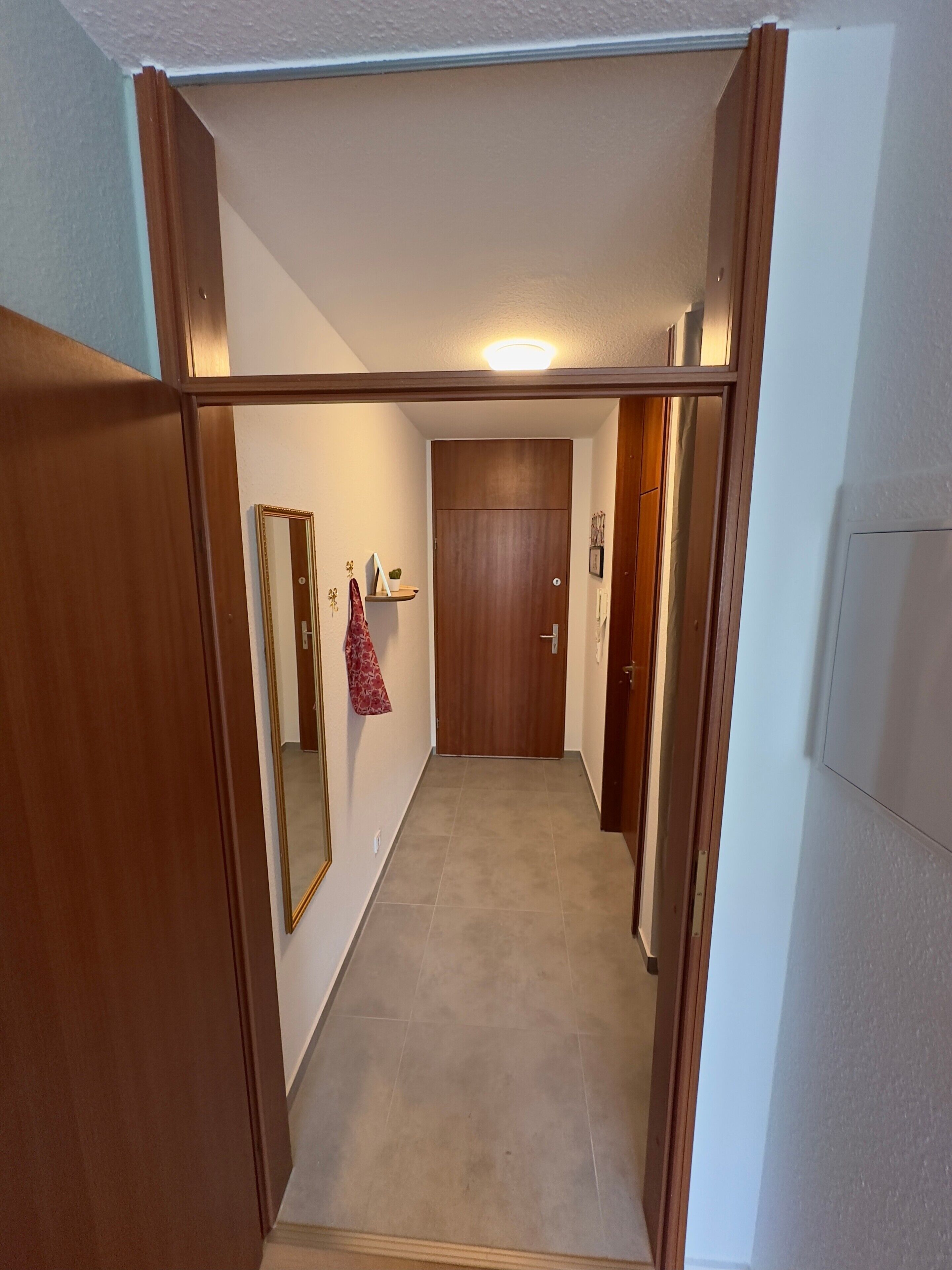 Un pasillo con una puerta de madera, un espejo y un pequeño estante con objetos.