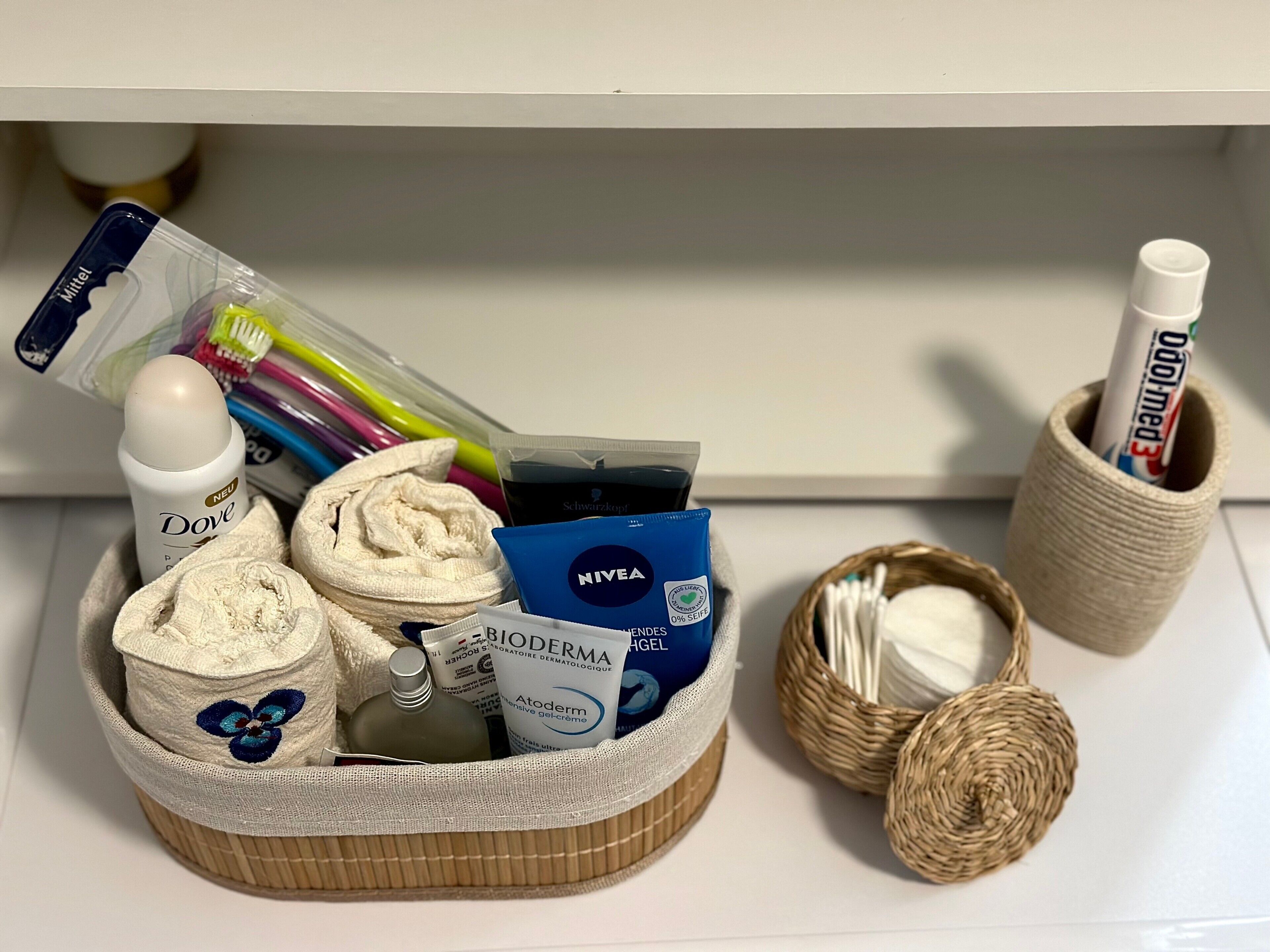 A bathroom with a white sink, a toothbrush holder with various toothbrushes, a bottle of Dove soap, a basket with toiletry items, and a wicker container with a white bottle.