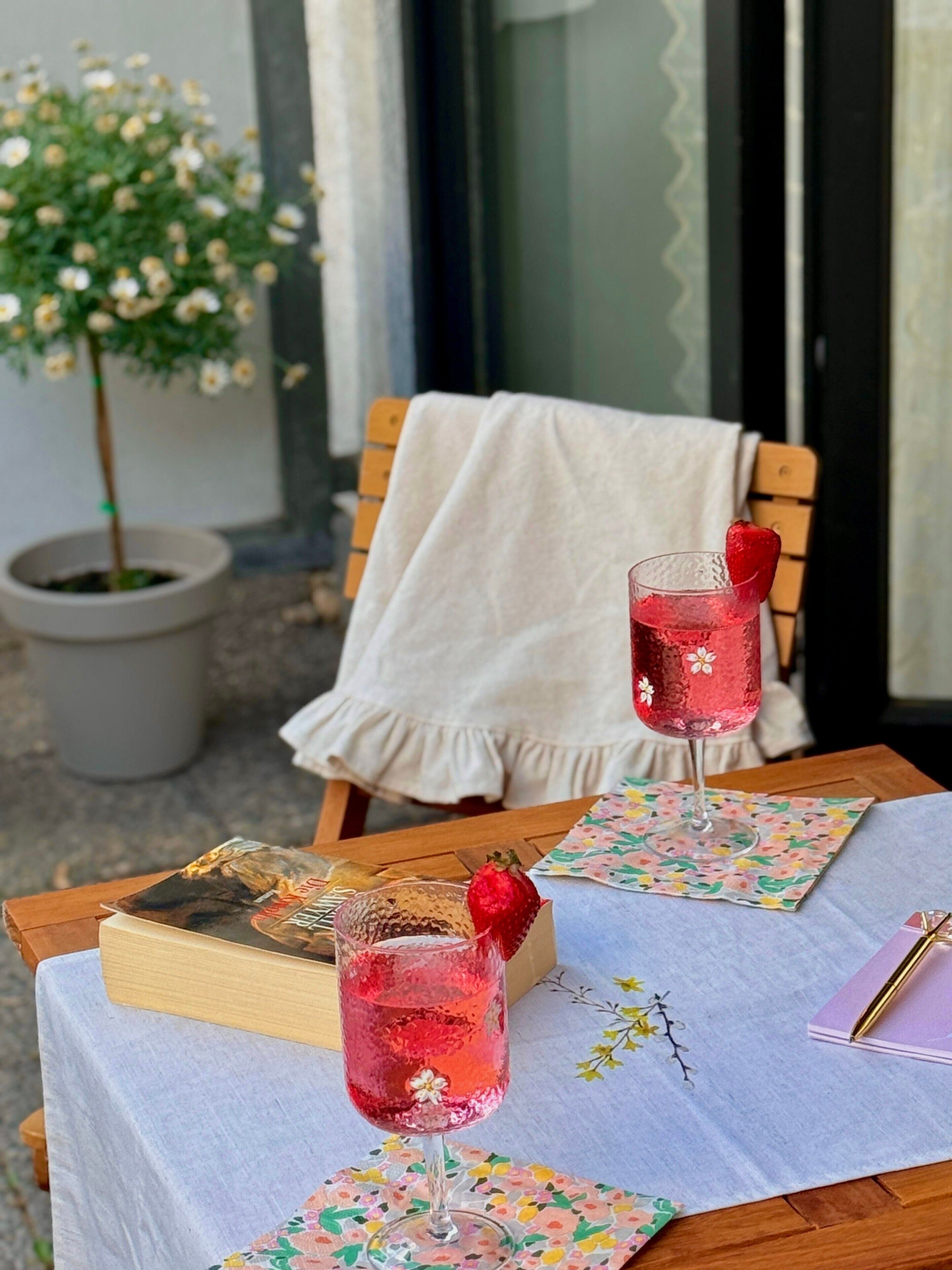 A table with two glasses of pink beverage, a book, and a notebook on a floral tablecloth.