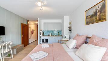 A bedroom with a bed, pillows, a bedside table, a TV, and a kitchen area with cabinets and a sink.