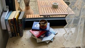 Vista desde la ventana de una estantería ordenada con libros, un adorno pequeño y una mesa con un tazón y una taza.
