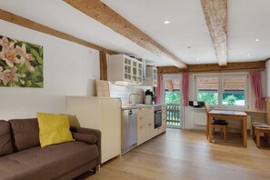 A kitchen with wooden beams, a dining area with a table and chairs, and a sofa with a yellow pillow.