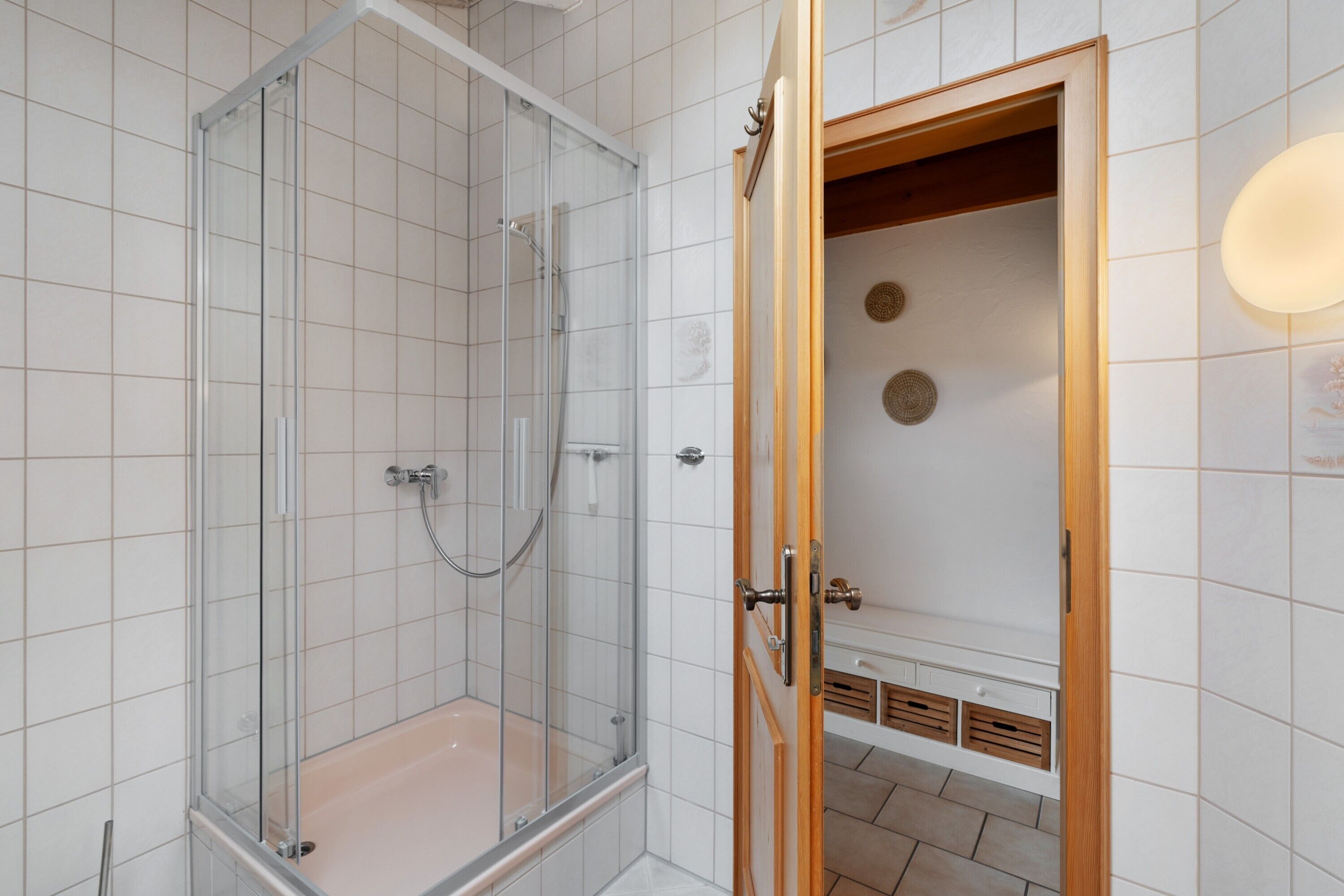 Een moderne badkamer met een glazen douchecabine, een houten deur en betegelde wanden.