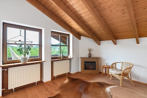 Una habitación con vigas de madera, chimenea, una silla de mimbre y vistas a través de amplios ventanales.