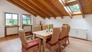 Un espace repas avec une table et des chaises en bois, de grandes fenêtres et un plafond en pente.