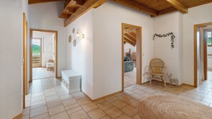 Une pièce spacieuse avec un plafond en bois, des murs blancs et un sol carrelé. On y trouve une chaise, une petite table et un élément décoratif mural.
