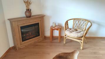 Een kamer met een open haard, een rieten stoel, een klein tafeltje en een hond die op de vloer ligt.