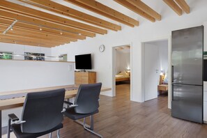 Une cuisine moderne dotée d’un réfrigérateur en acier inoxydable, de poutres en bois au plafond et d’un coin repas avec deux chaises.