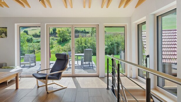 Un intérieur moderne avec un plafond en bois, de grandes portes-fenêtres coulissantes, une chaise noire et une table en bois.