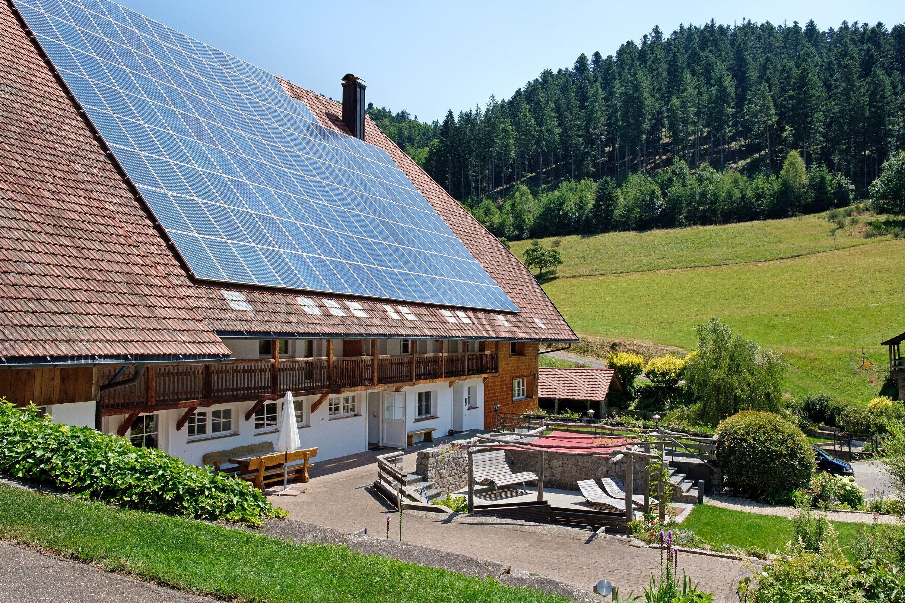 Ein Gebäude mit geneigtem Dach, Solaranlagen, einem Balkon und einem Garten.