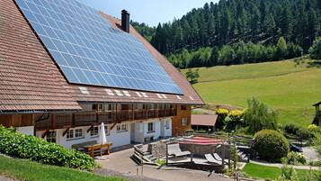 Ein Gebäude mit geneigtem Dach, Solaranlagen, einem Balkon und einem Garten.