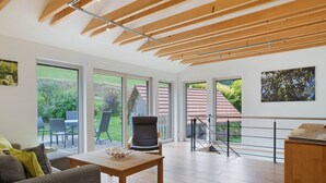 Une pièce spacieuse avec de grandes fenêtres, un plafond en bois et une vue sur un jardin.