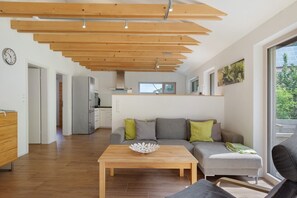 Ein moderner Wohnbereich mit Holzboden, einer Couch mit Kissen, einem Couchtisch und einer Küche im Hintergrund.