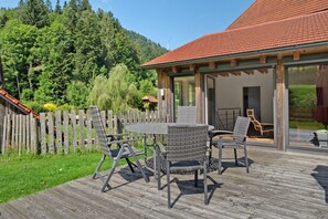 Une terrasse extérieure avec une table et des chaises, une clôture en bois et un bâtiment avec un toit rouge.