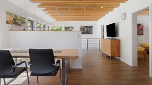 Un intérieur moderne avec un plafond en bois, un coin repas avec des chaises, un téléviseur et un meuble en bois.