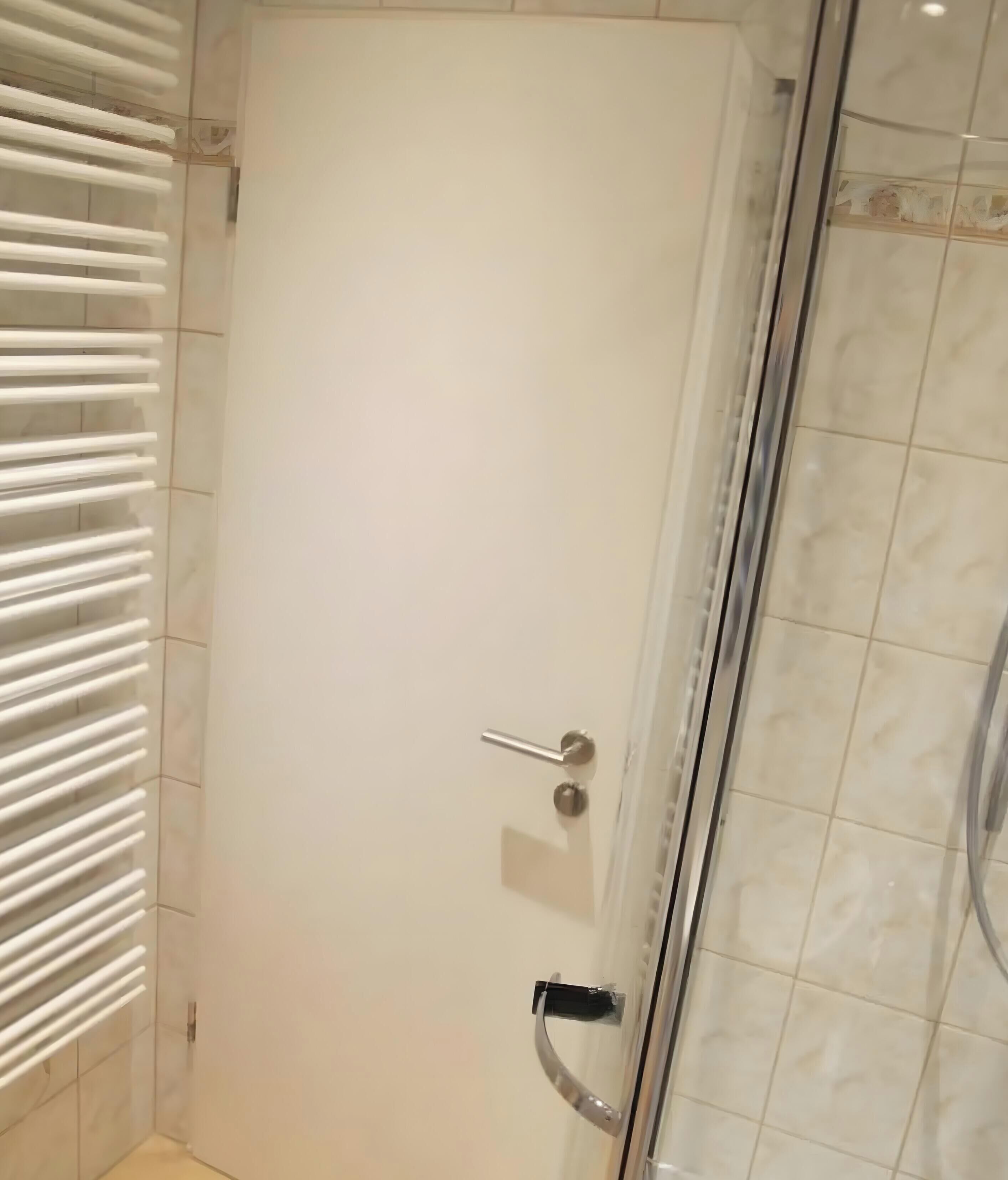Une salle de bain avec une porte blanche, une douche en verre et un porte-serviettes avec des serviettes blanches.