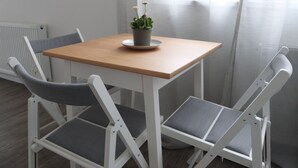 Ein kleiner, quadratischer Holztisch mit einem Blumentopf, umgeben von zwei weißen Stühlen mit grauen Kissen.