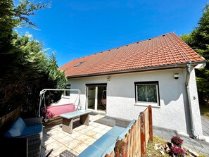 A house with a red-tiled roof, a covered patio with outdoor furniture, and a small garden area.