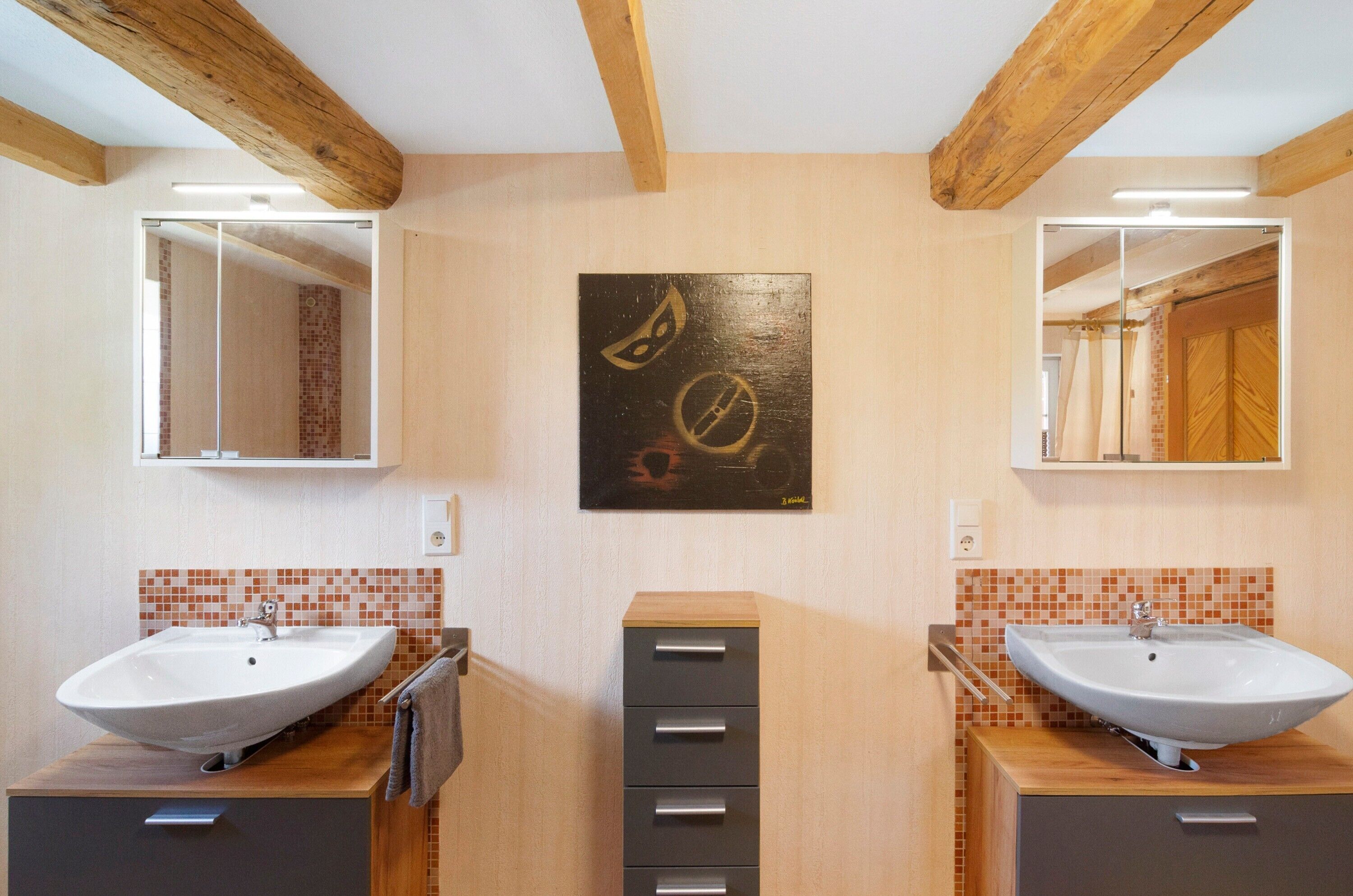 A bathroom with two sinks, a mirror, a cabinet, and a wall-mounted artwork.