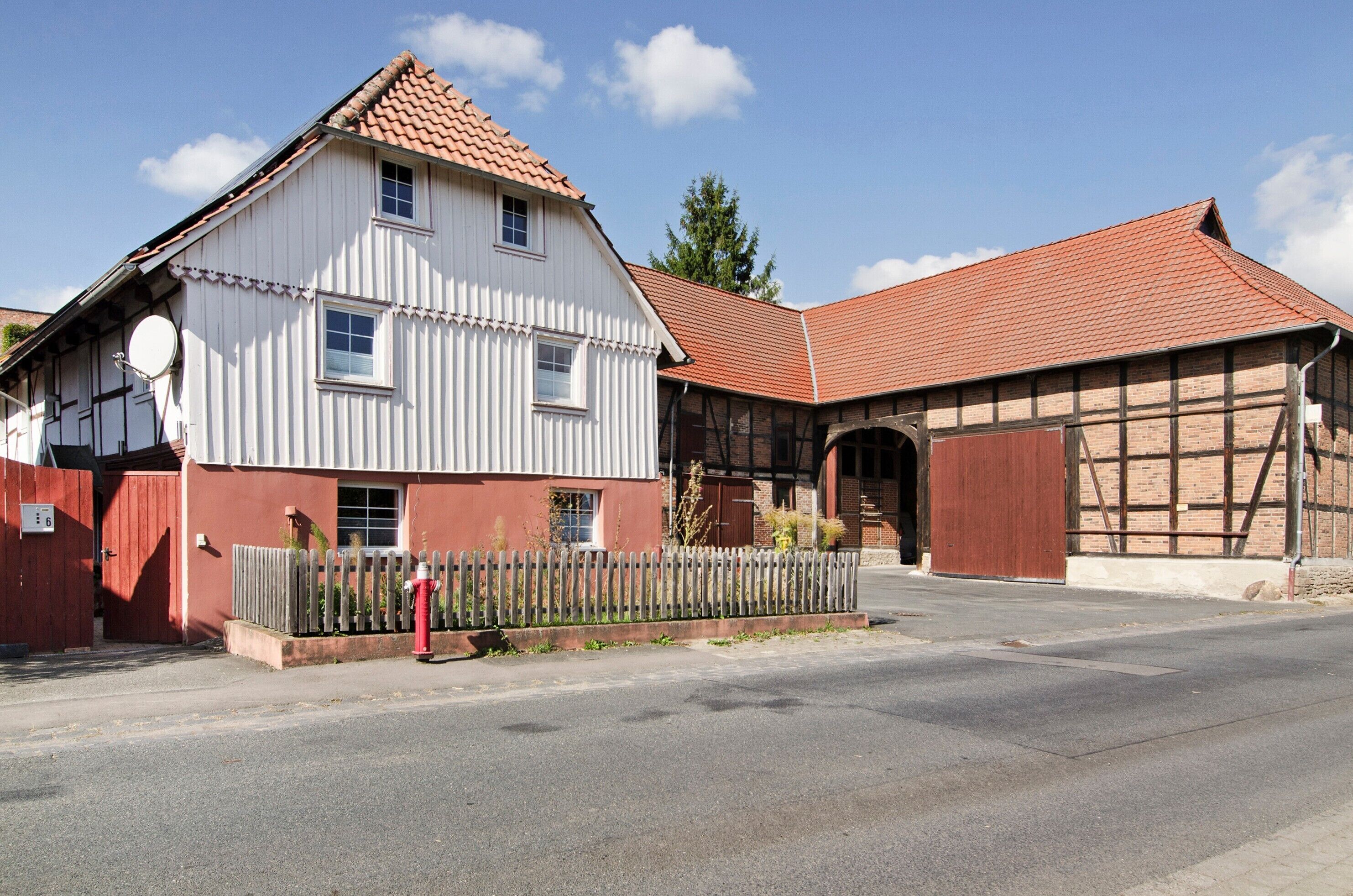 A traditional building with a red-tiled roof, a white facade, and a wooden fence in front.