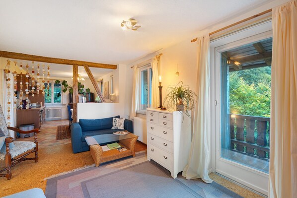 A cozy living room with a blue sofa, a white dresser, and a large window with a view of greenery.