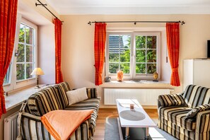 Una habitació amb dos sofàs estripats, una taula, un radiador i una finestra amb cortines.