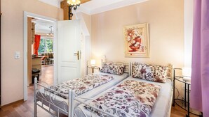 A bedroom with two beds, a chandelier, a painting, and a door leading to another room.