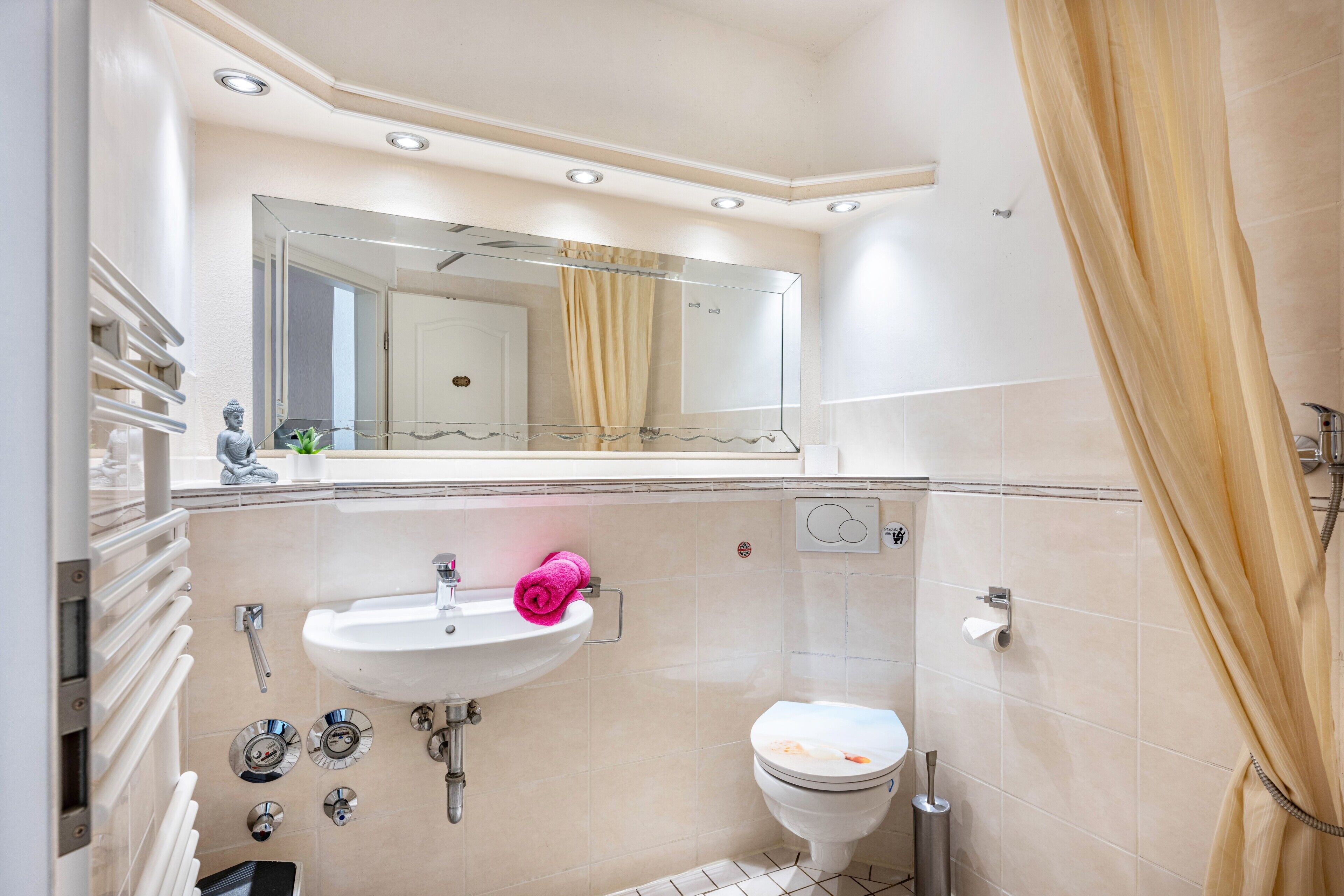 A bathroom with a sink, mirror, toilet, shower curtain, and towel rack.