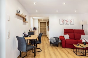Een moderne woonkamer met een rode bank, een eettafel met stoelen, en een keuken op de achtergrond.
