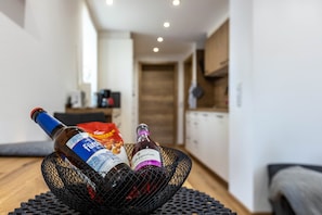 Eine Flasche Fuzzy's Bier, eine Flasche Apfelwein und eine Tüte Fuzzy's Nüsse in einem schwarzen Netzkorb auf einem Holztisch in einer modernen Küche mit Holzboden und weißen Wänden.