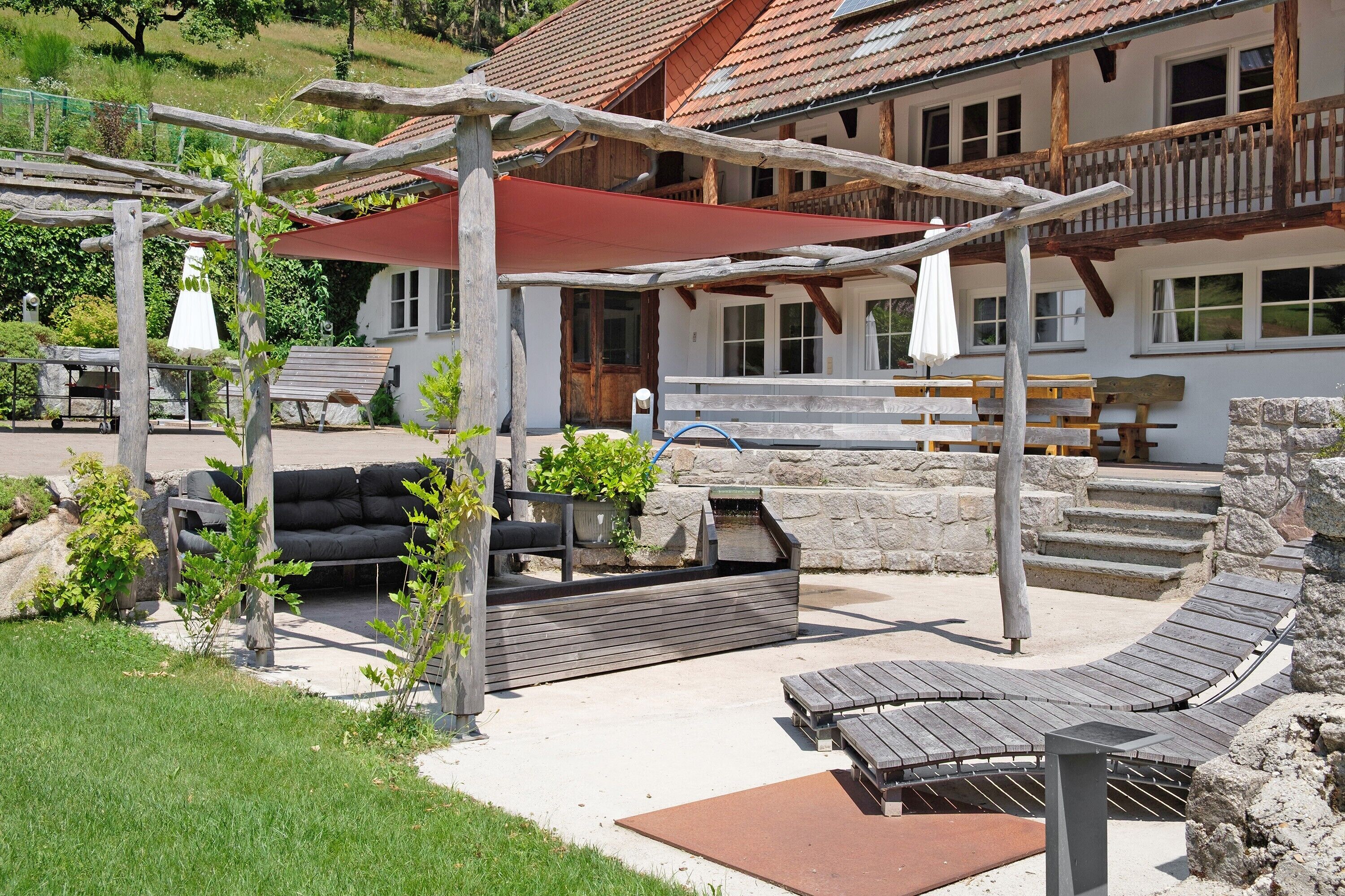 A patio with wooden furniture, a barbecue, and a stone wall.