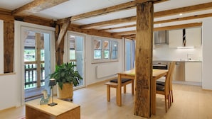 A spacious living area with wooden beams, a dining table, chairs, a potted plant, and a kitchen in the background. - Apartment 'Mühlenstüble' with Mountain View, Shared Terrace and Wi-Fi (Gutach (Schwarzwaldbahn))