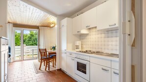 A modern kitchen with white cabinets, a built-in oven, and a dining area with a table and chairs. - Apartment 'Ella Walter, Kiek Ut' with Private Terrace, Shared Garden and Wi-Fi (Nordstrand)