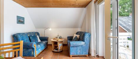 A room with two patterned sofas, a wooden table, a small round side table, and a large sliding glass door leading to an outdoor area.